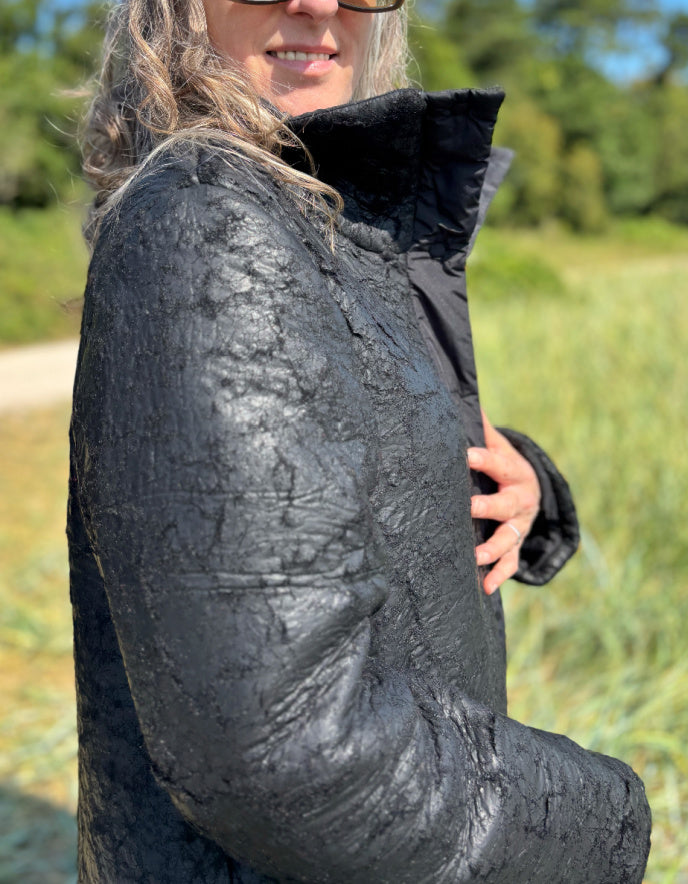 Person wearing a black textured jacket outdoors with greenery in the background
