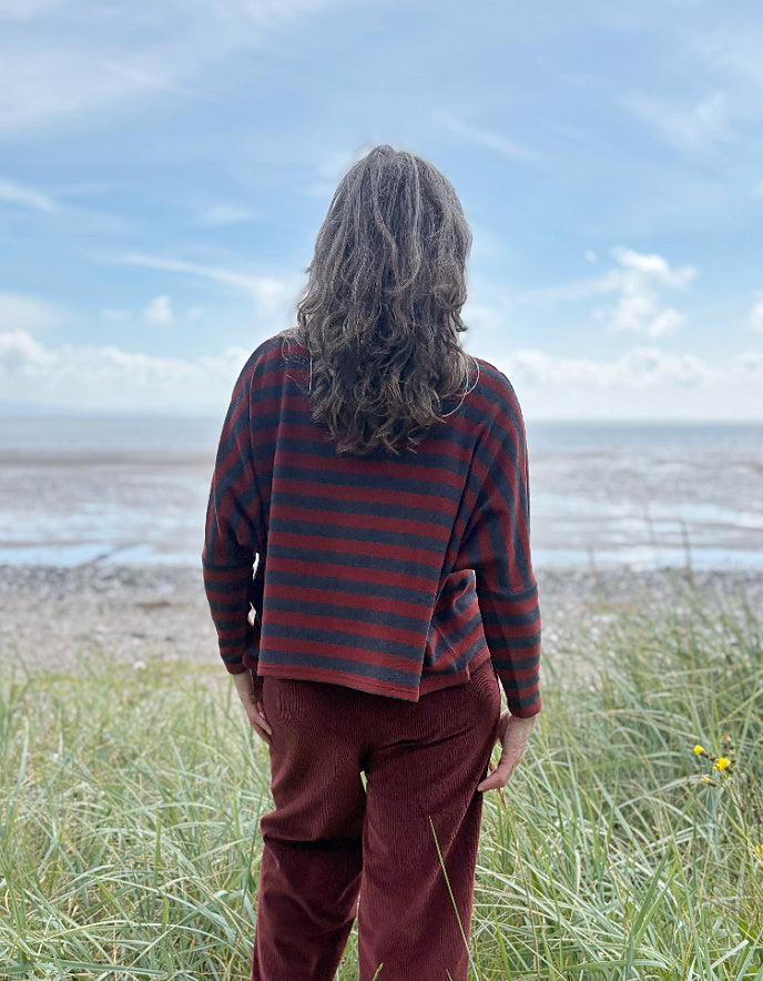 Person wearing a copper and charcoal striped turtle neck sweater with copper corduroy wide leg trousers and sunglasses on a beach