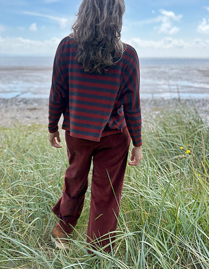 Person wearing a copper and charcoal striped turtle neck sweater with copper corduroy wide leg trousers and sunglasses on a beach