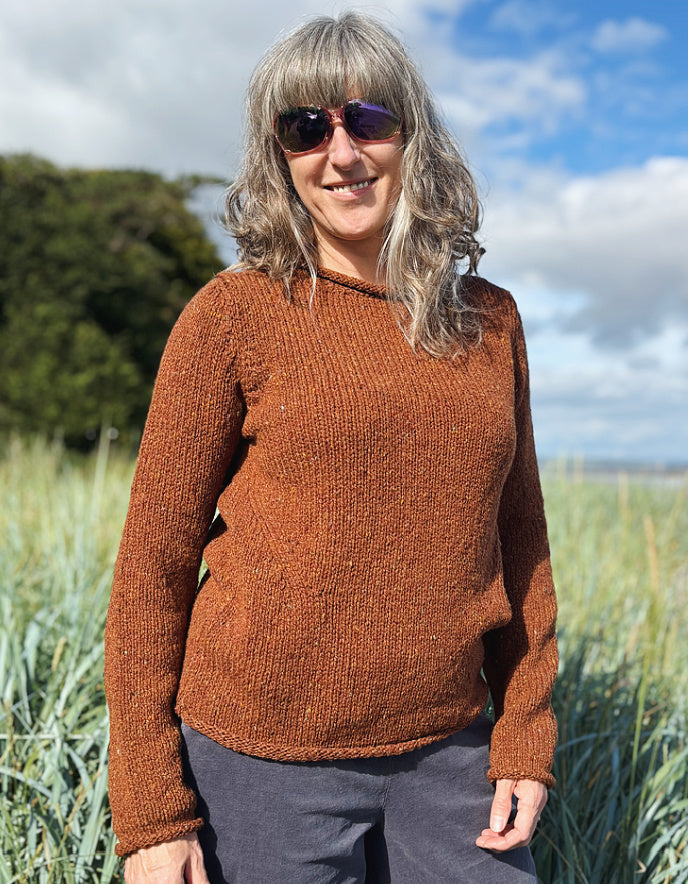 Woman wearing a coper brown donegal tweed sweater standing in a field with a scenic background