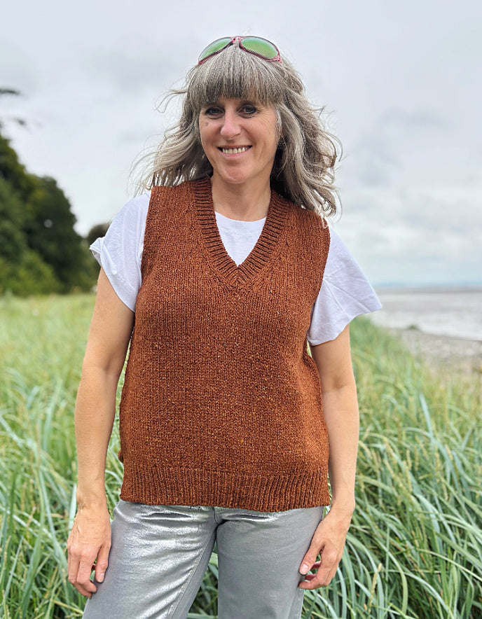 Woman wearing a brown donegal tweed knitted vest over a white shirt in a grassy field.