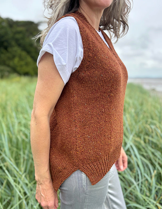 Woman wearing a brown donegal tweed knitted vest over a white shirt in a grassy field.