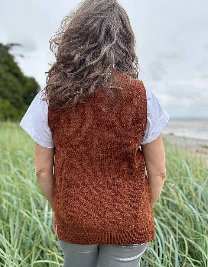 Woman wearing a brown donegal tweed knitted vest over a white shirt in a grassy field.