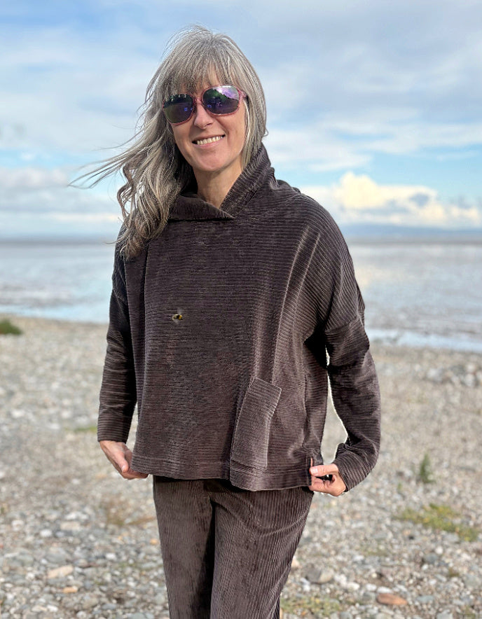 Person wearing a brown cord hooded sweater on a beach with ocean and sky in the background