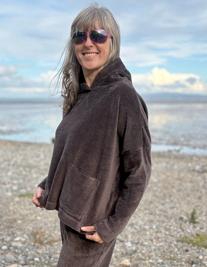 Person wearing a brown cord hooded sweater on a beach with ocean and sky in the background
