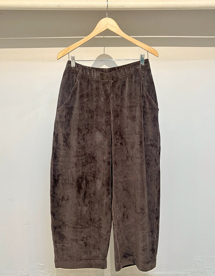Brown corduroy pants hanging on a wooden hanger against a white background
