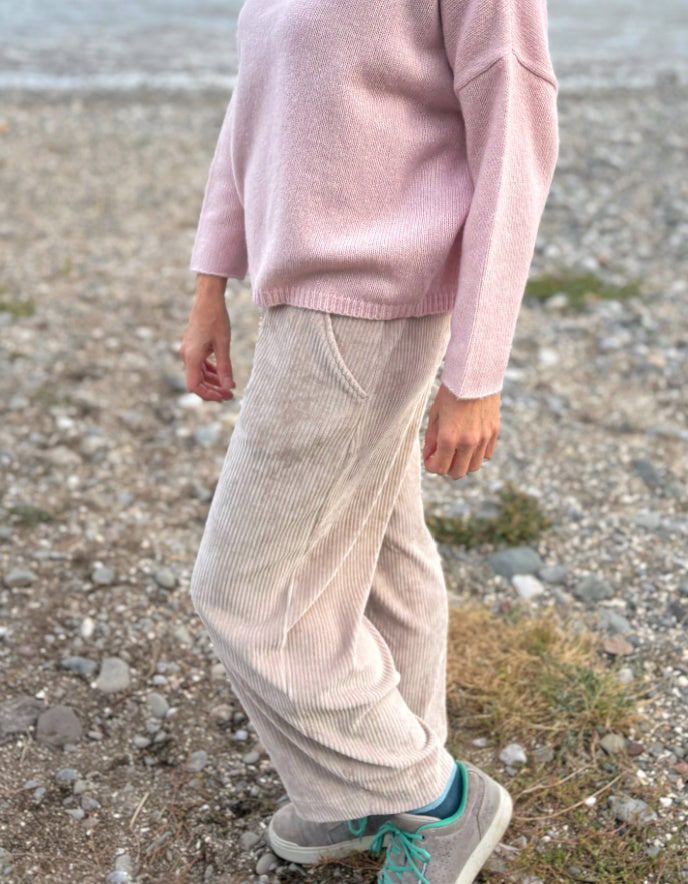 Person wearing a pink sweater and beige pants standing on a rocky surface.