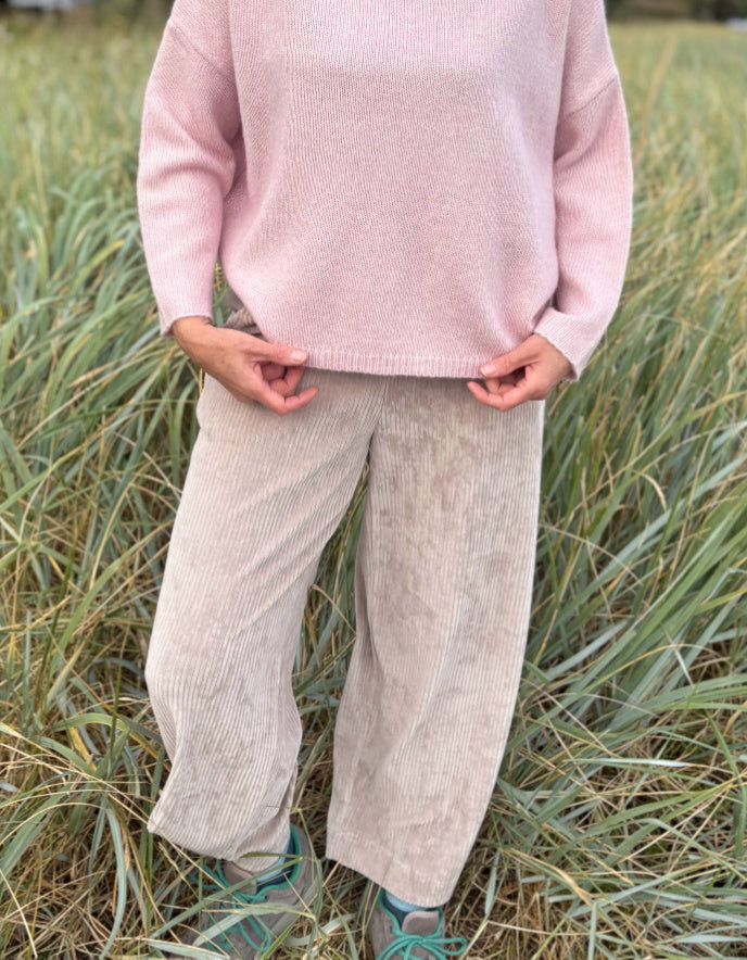 Person wearing a pink sweater and beige pants standing in a grassy field