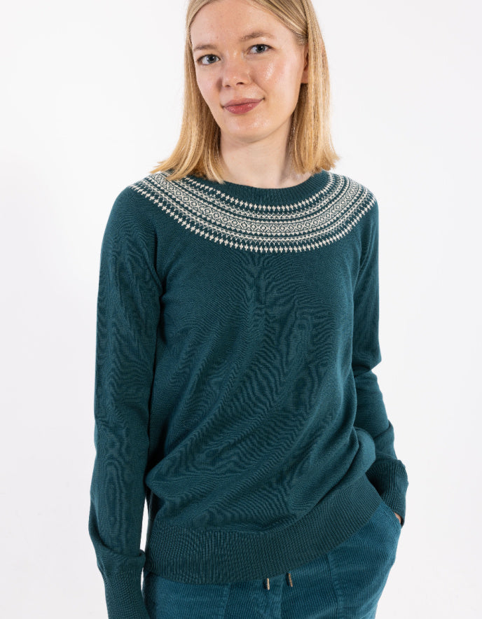Person wearing a teal sweater with intricate patterns on a white background