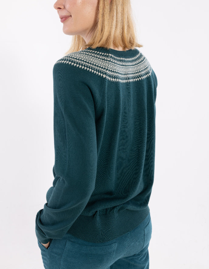Person wearing a teal sweater with a patterned neckline on a white background