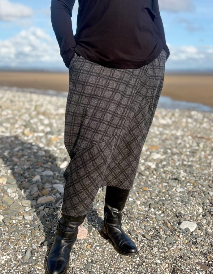 Person wearing a plaid skirt and boots standing on a beach.