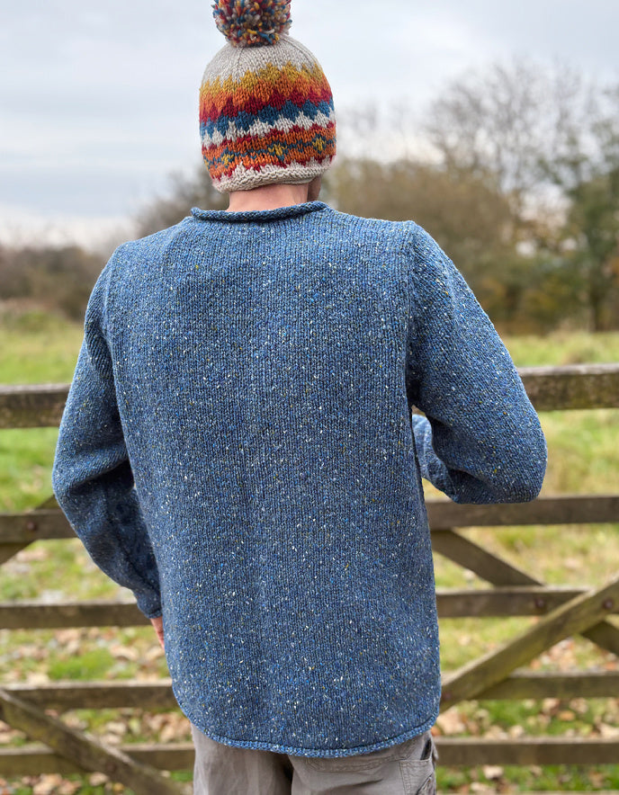 Person wearing a blue knitted sweater and colorful beanie standing in a field.