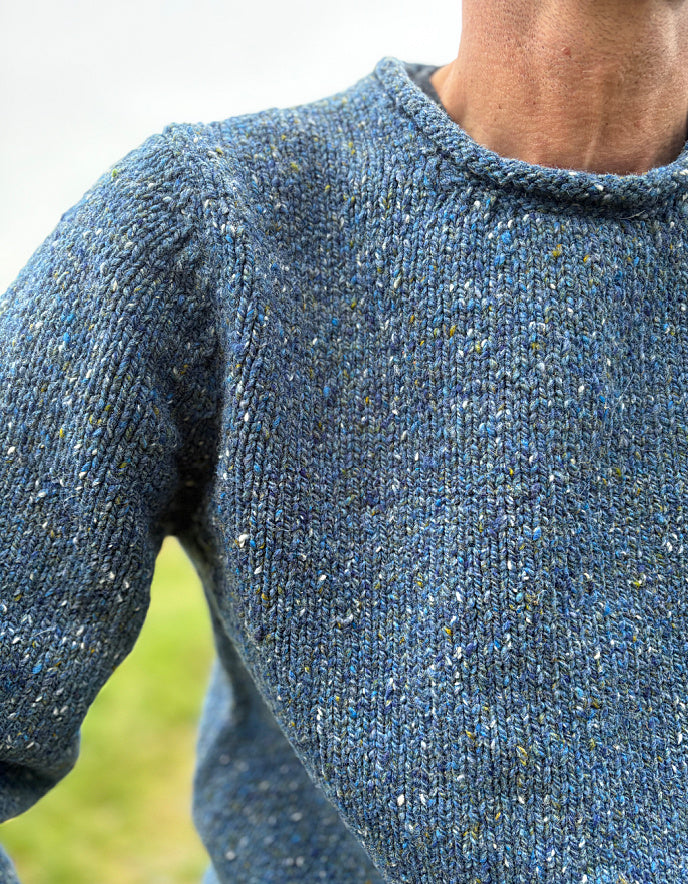 Close-up of a person wearing a blue knitted sweater with a blurred green background