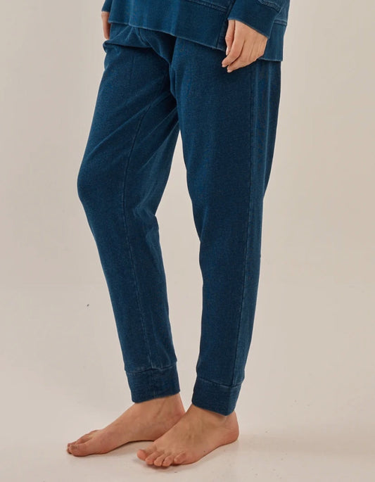 A person wearing dark blue jogger-style pants with a relaxed fit and cuffed ankles, shown from the waist down against a plain light beige studio background.