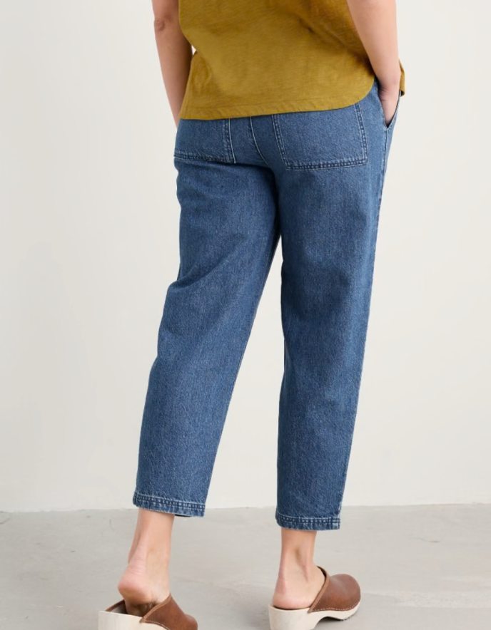 Person wearing a mustard yellow cardigan and blue jogger style jeans on a white background