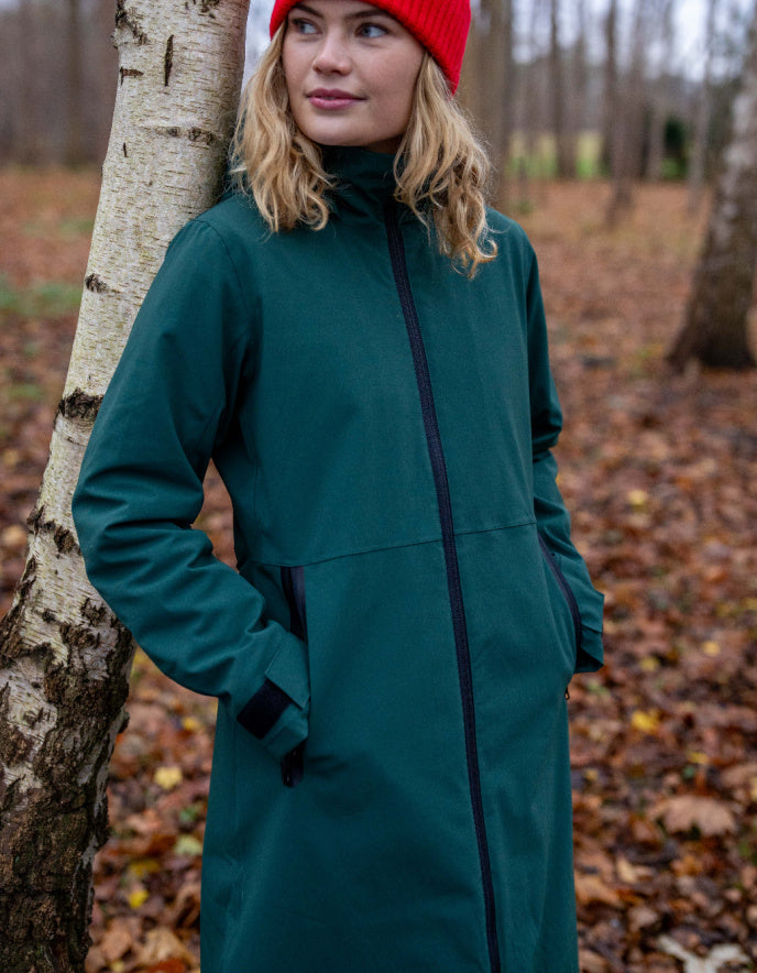 Person wearing a teal coat standing next to a tree in a forest setting