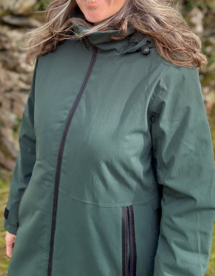 Person wearing a green jacket with a stone wall background