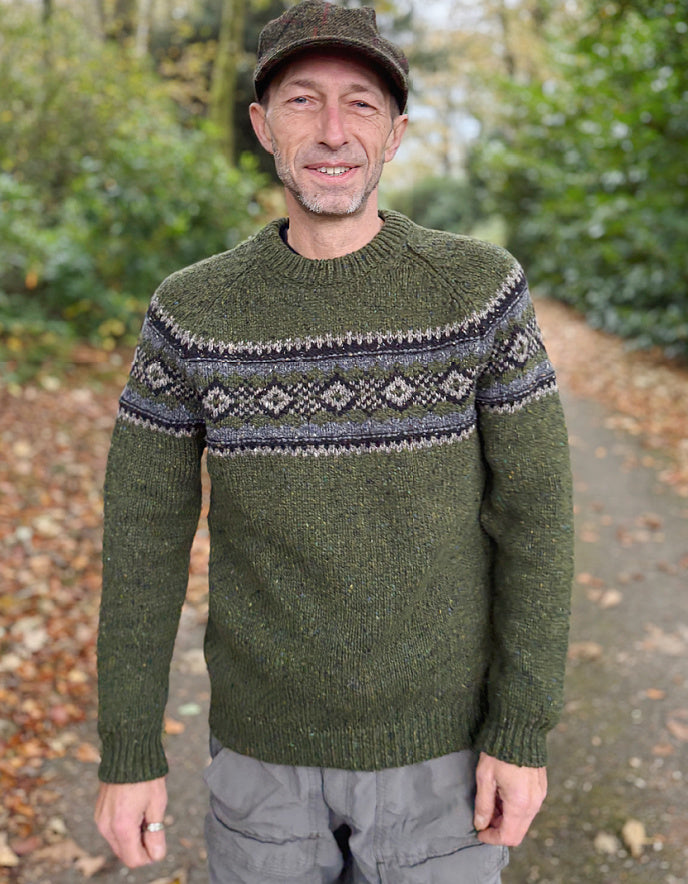 Man wearing a green knitted sweater with a patterned design outdoors.