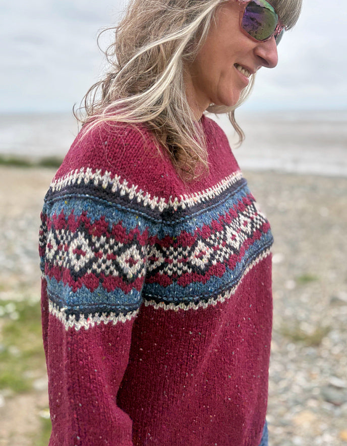 Person wearing a red Fair Isle patterned sweater standing in a grassy field