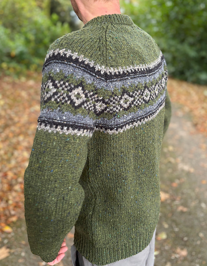 Green knitted sweater with a patterned yoke worn by a person outdoors.