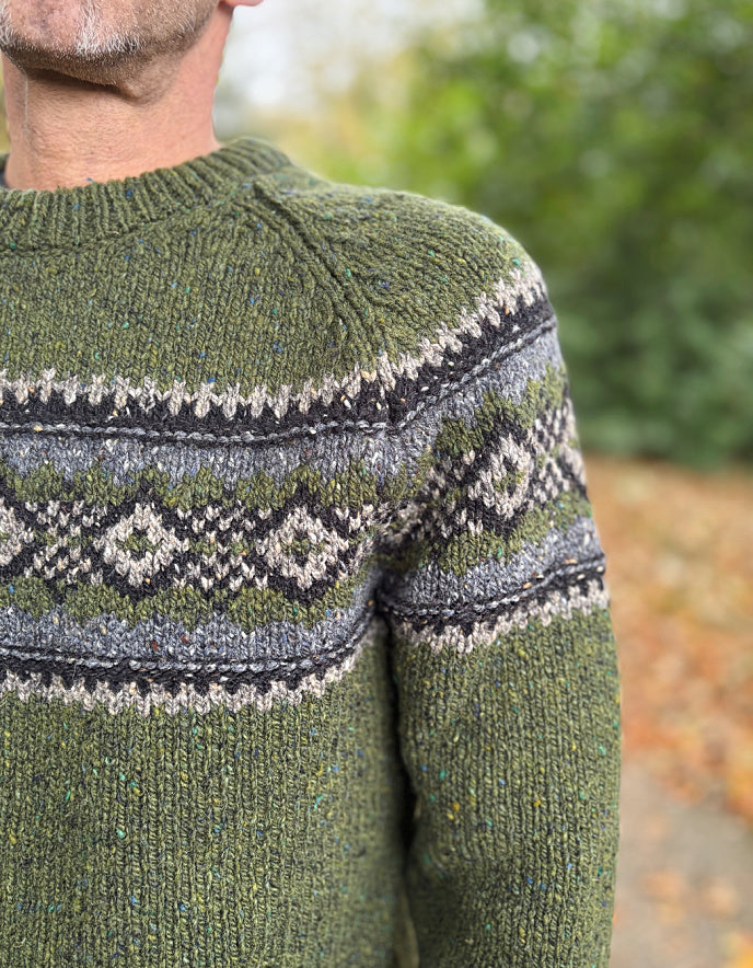Green knitted sweater with a patterned collar worn by a person, outdoors.