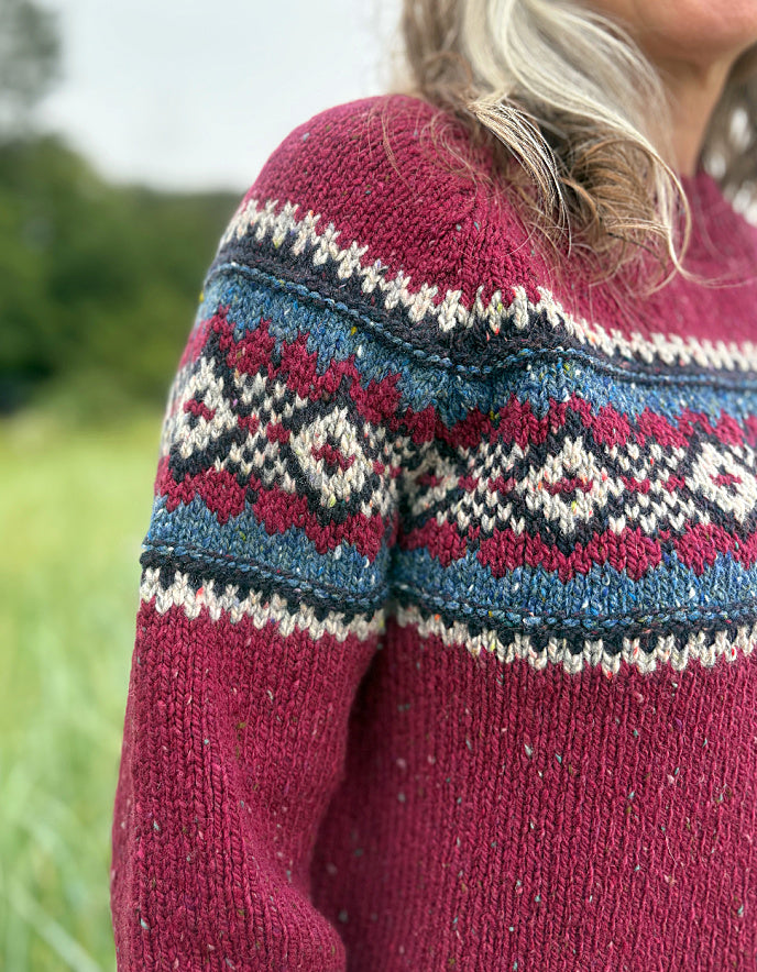 Person wearing a red Fair Isle patterned sweater standing in a grassy field
