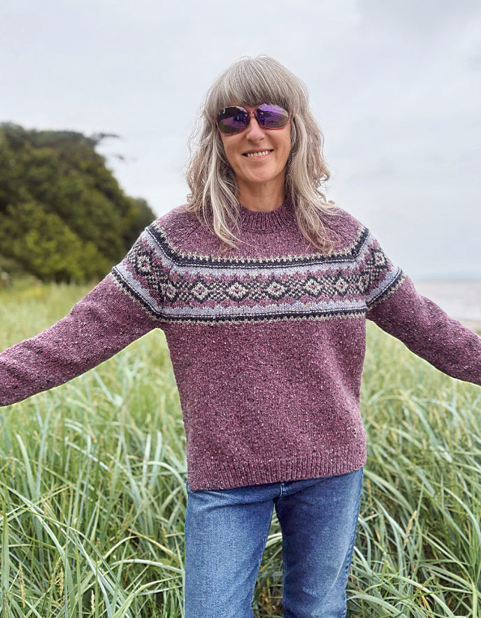 Person wearing a patterned berry Fair Isle sweater and sunglasses in a field