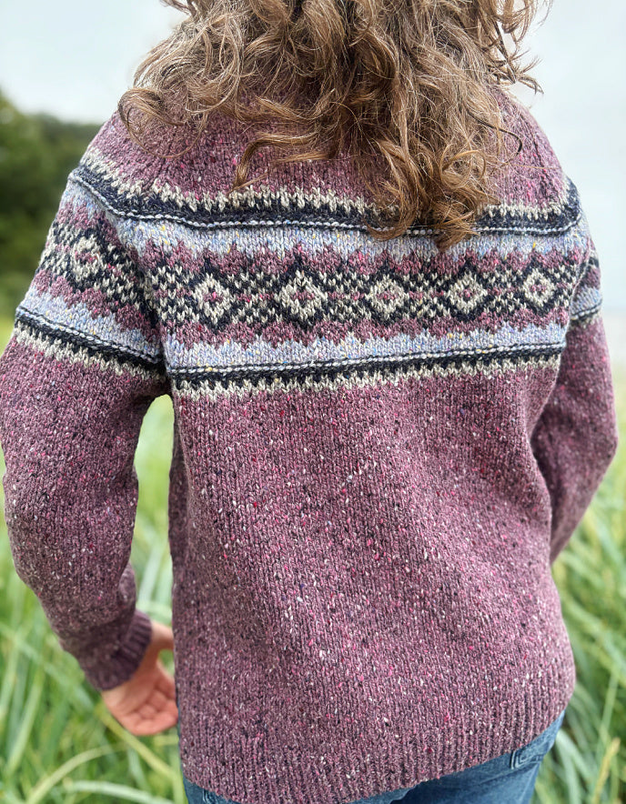 Person wearing a patterned berry Fair Isle sweater and sunglasses in a field
