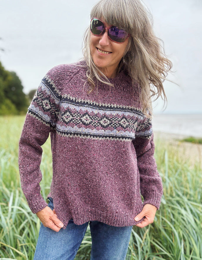 Person wearing a patterned berry Fair Isle sweater and sunglasses in a field