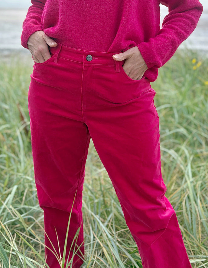 Person wearing bright pink velvet pants and a matching top standing in grass.