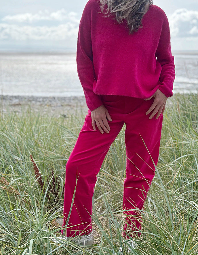 Person wearing bright pink velvet pants and a matching top standing in grass.