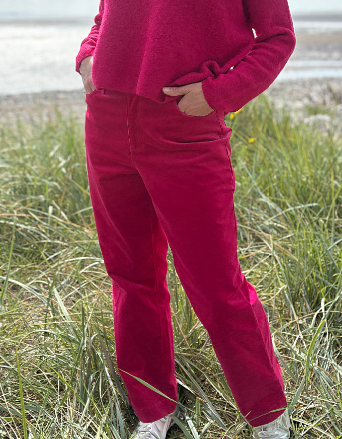 Person wearing bright pink velvet pants and a matching top standing in grass.