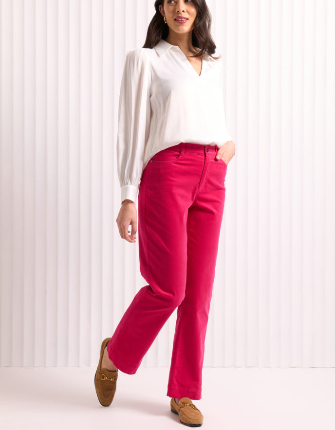 Woman wearing a white blouse and bright pink velvet pants against a white background