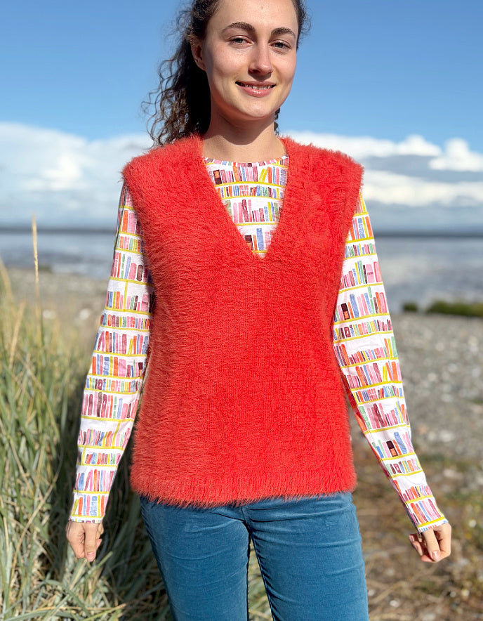 Person wearing an orange fluffy knitted vest over a colourful patterned shirt on a beach.