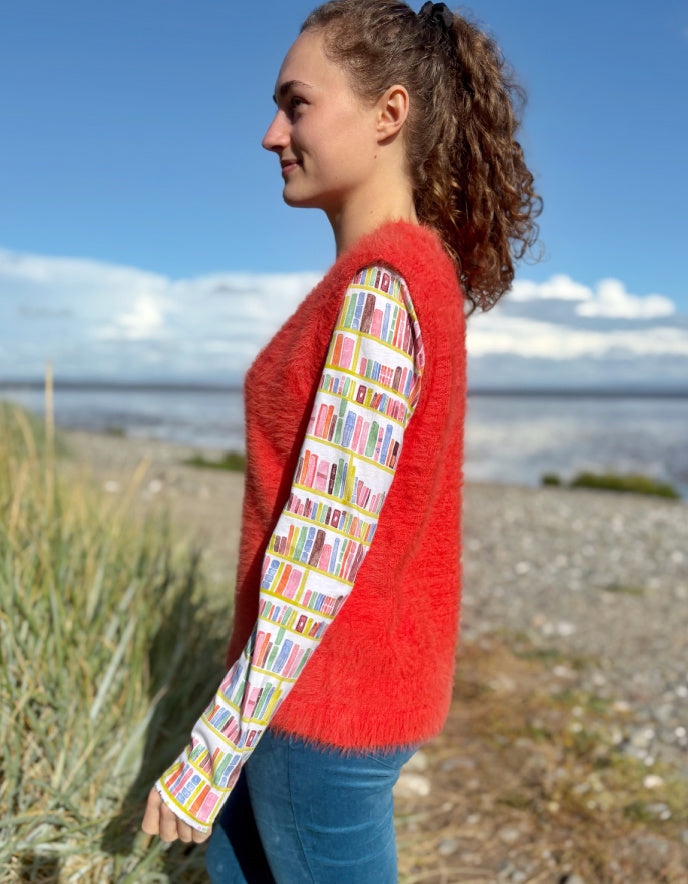 Person wearing an orange fluffy knitted vest over a colourful patterned shirt on a beach.