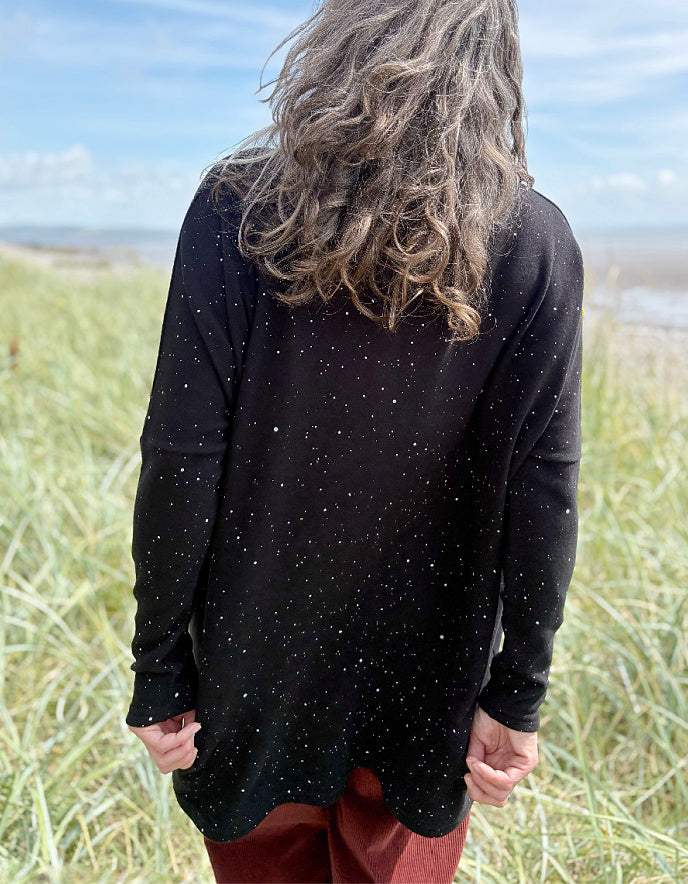 Person standing in a grassy field with a scenic background wearing a black cosy turtle neck tunic and copper brown cord trousers