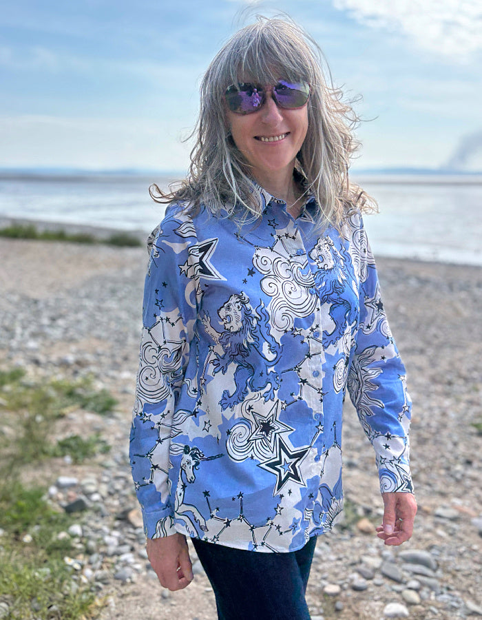 Person wearing a blue patterned shirt standing on a beach with ocean and sky in the background