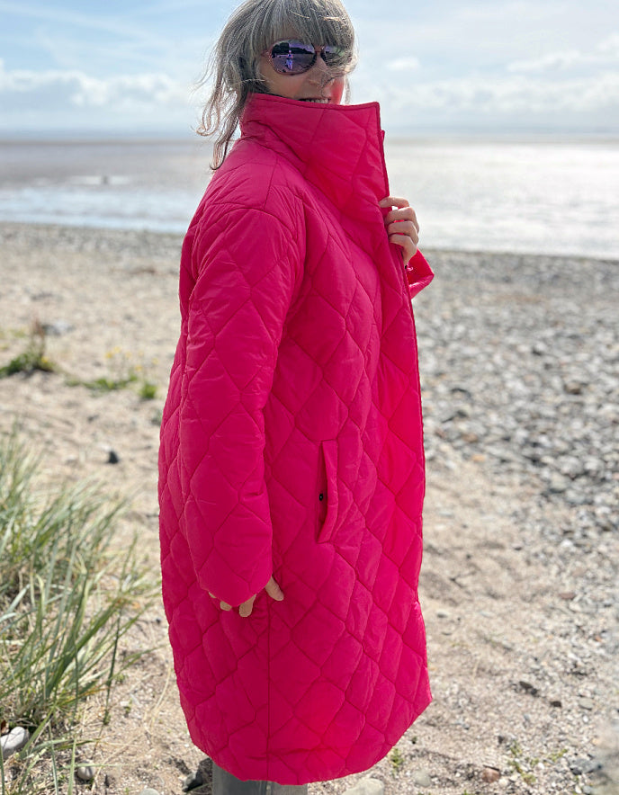 Person wearing a bright pink quilted coat on a beach