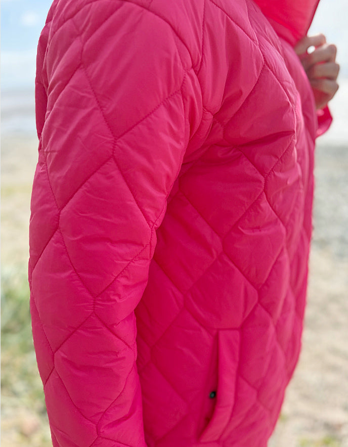 Close-up of a bright pink quilted jacket with a blurred natural background