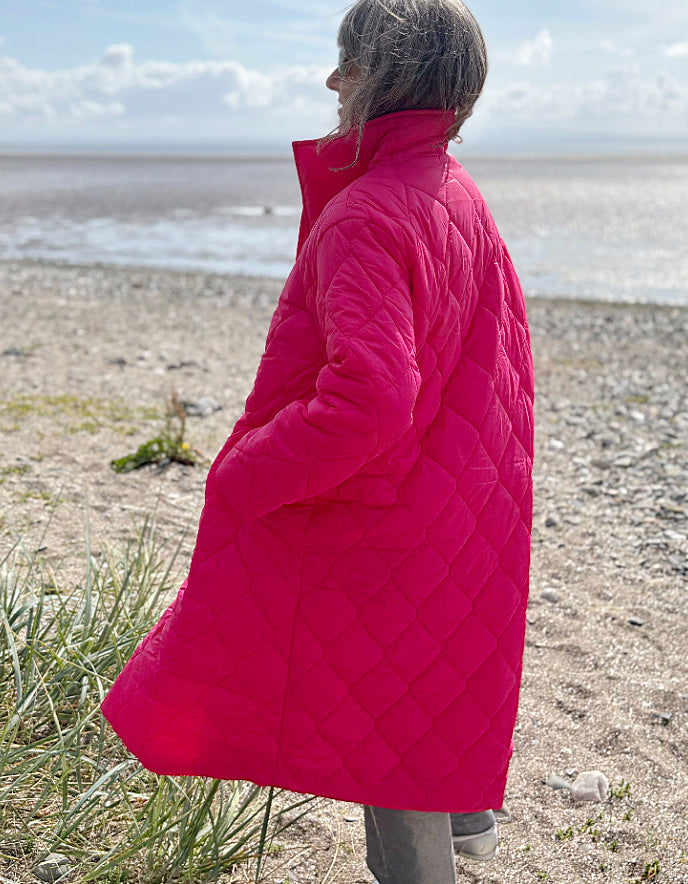 Person wearing a bright pink quilted coat standing on a beach.
