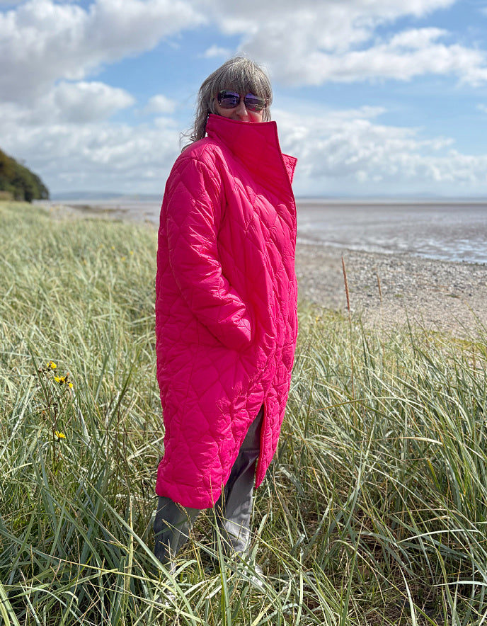 Woman wearing a bright pink midi length puffer coat against a natural background