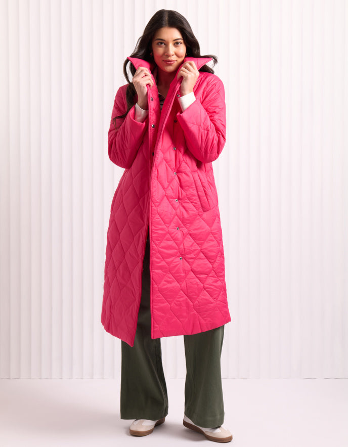 Woman wearing a bright pink midi length puffer coat against a white background