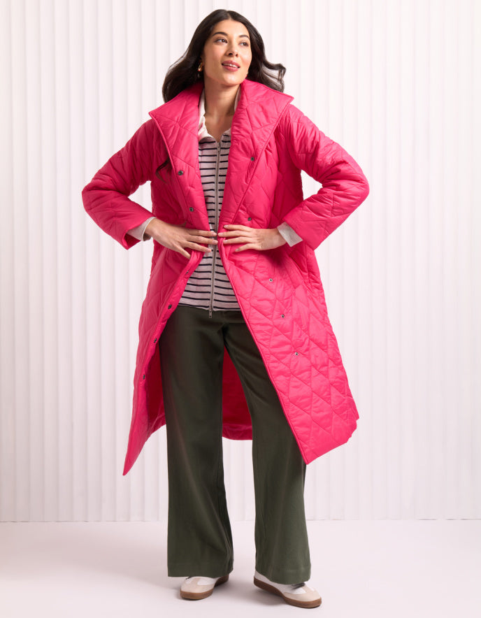 Woman wearing a bright pink midi length puffer coat against a white background