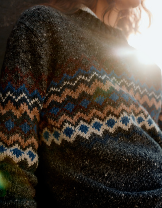Woman wearing a dark grey tweed sweater with fair isle patterned against a white background