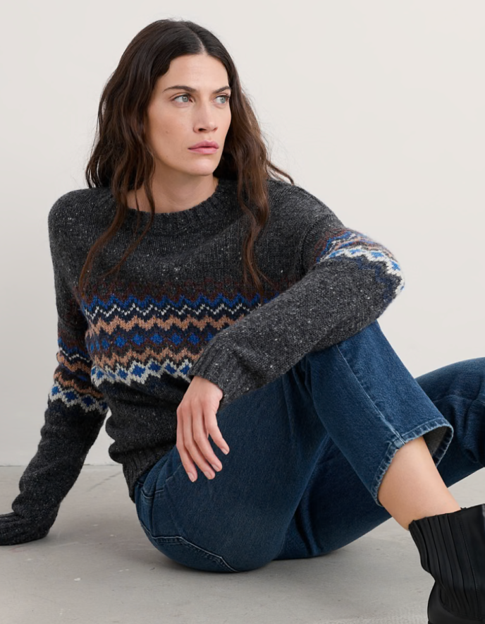 Woman wearing a dark grey tweed sweater with fair isle patterned against a white background