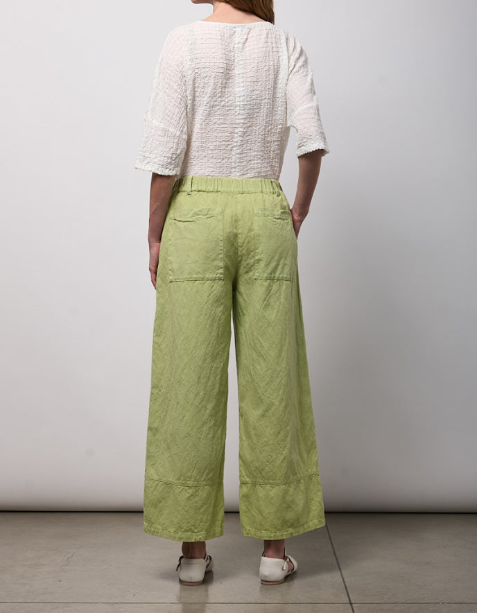 Person wearing a white top and green wide-leg pants against a plain background