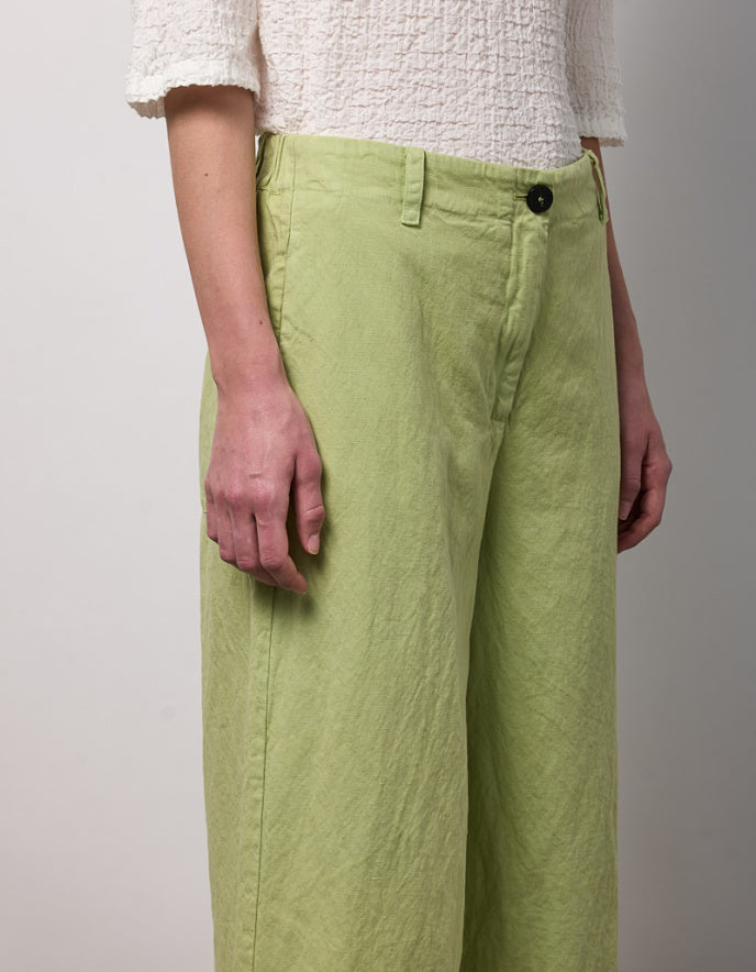 Person wearing light green pants and a white textured shirt on a plain background