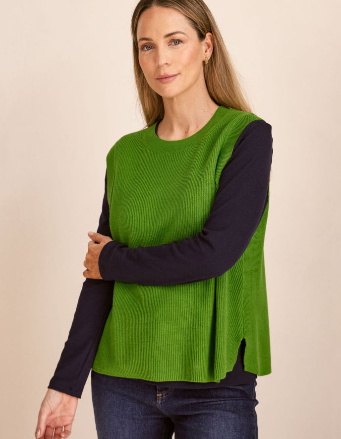 Woman wearing a green cotton tank top over a dark long-sleeve shirt on a beige background