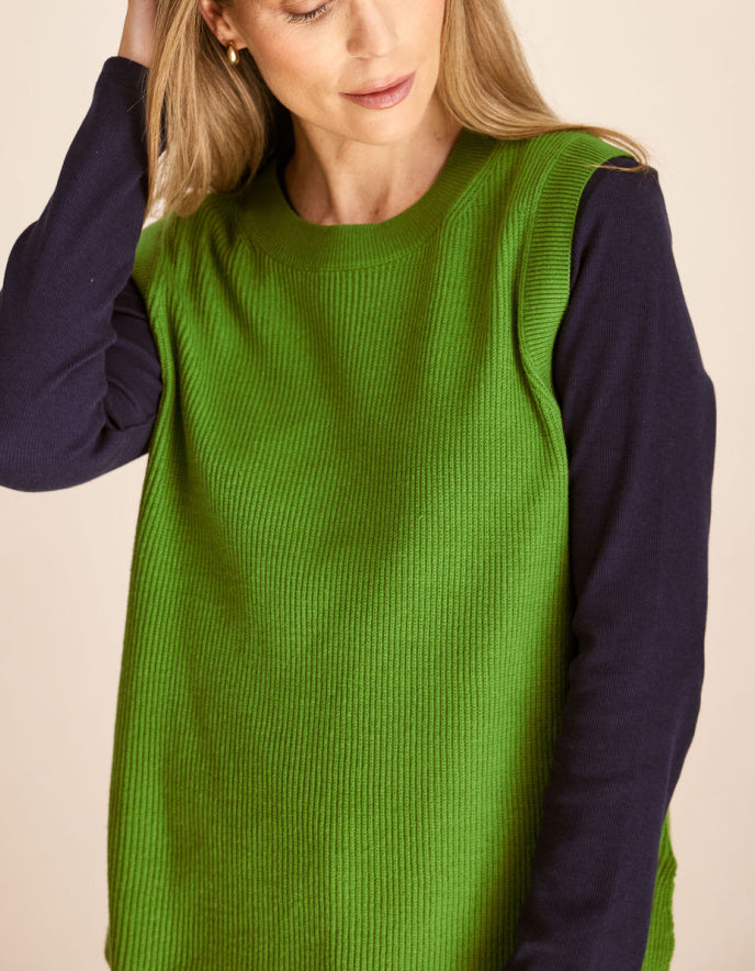 Woman wearing a green cotton tank top over a dark long-sleeve shirt on a beige background