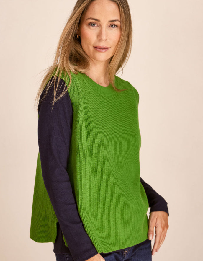 Woman wearing a green cotton tank top over a dark long-sleeve shirt on a beige background